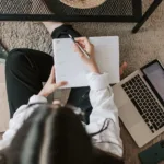 faceless lady with notebook and laptop on floor at home
